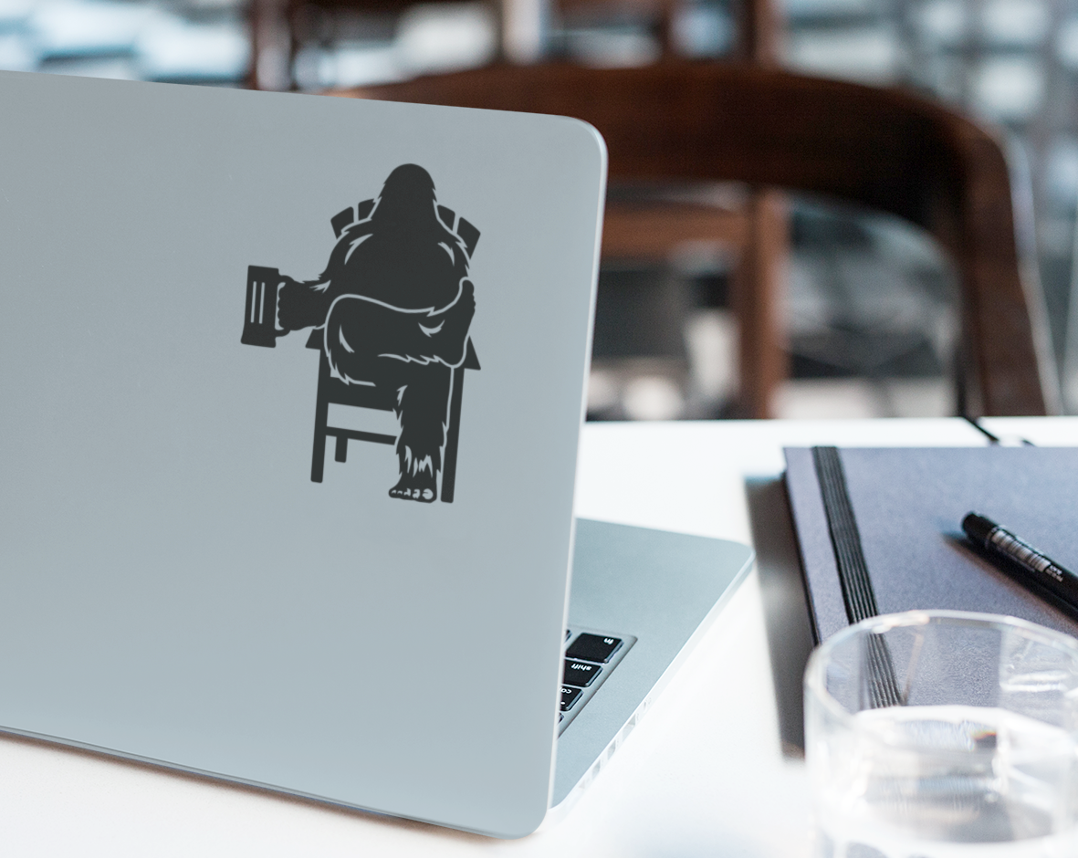 Laptop computer with black decal of Bigfoot relaxing in a chair, holding a beer mug.