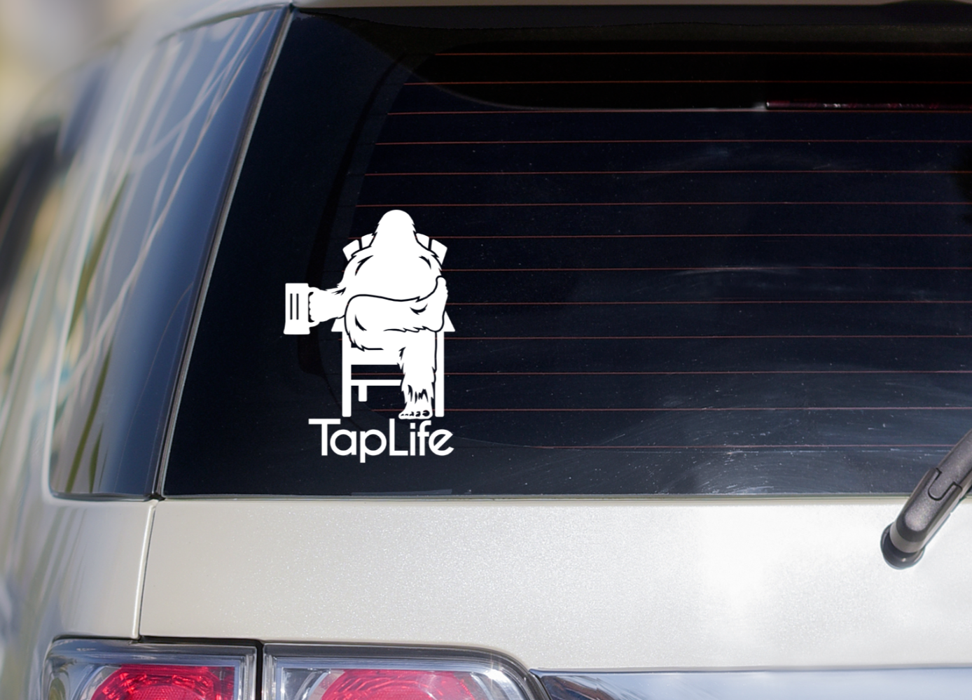 Rear window of van with decal of Bigfoot, holding a beer mug and relaxing in a chair, with Tap Life logo below.