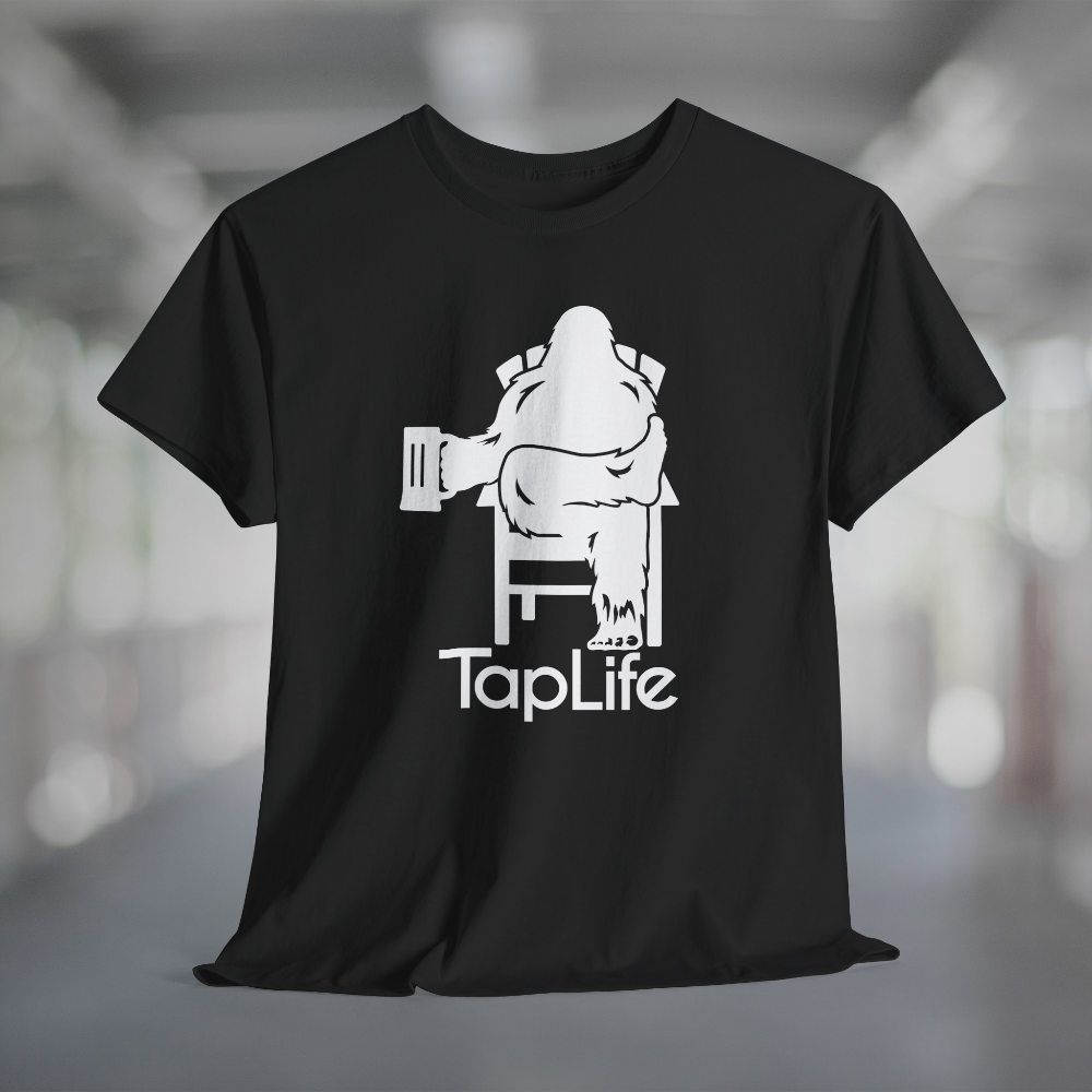 Black t-shirt with white graphic of Bigfoot holding a beer mug, sitting in a lawn chair with leg crossed in relaxed position, Tap Life logo below.