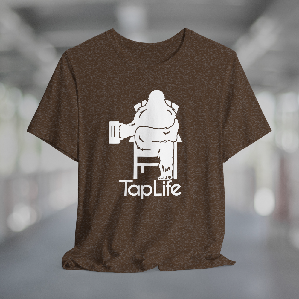Heather brown t-shirt with white graphic of Bigfoot holding a beer mug, sitting in a lawn chair with leg crossed in relaxed position, Tap Life logo below.