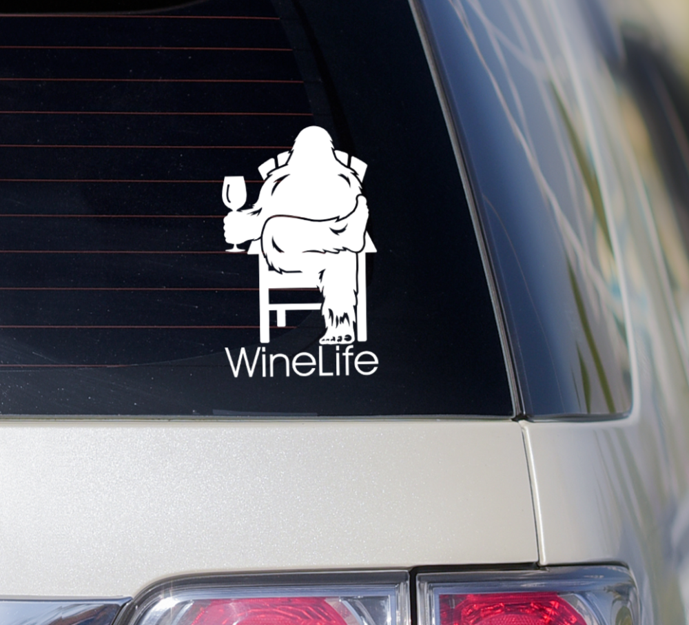 Rear window of car with decal of Bigfoot relaxing in a chair, enjoying a glass of wine, Wine Life logo below.