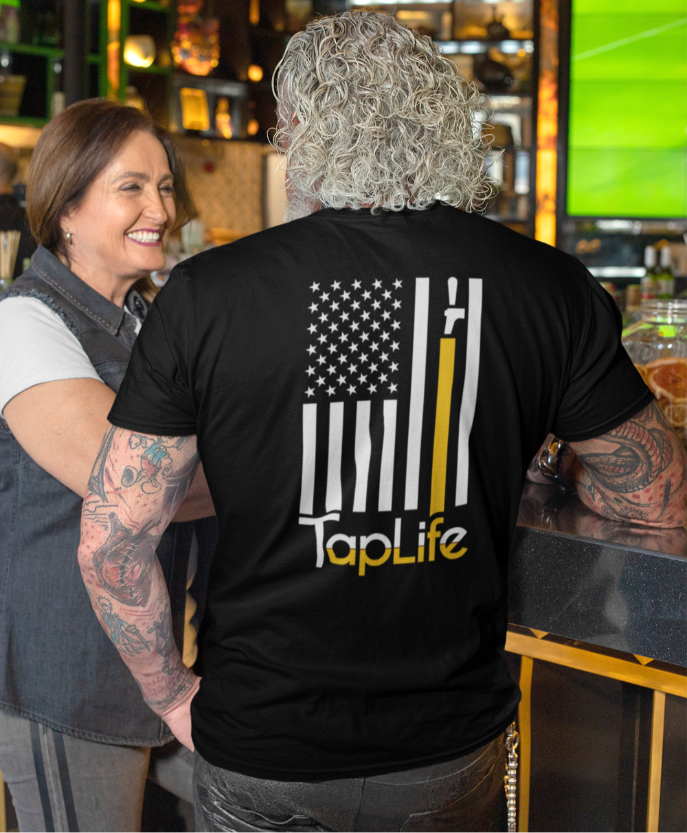 Man wearing black t-shirt with print of American flag, with one stripe yellow pouring from a beer tap, Tap Life logo below