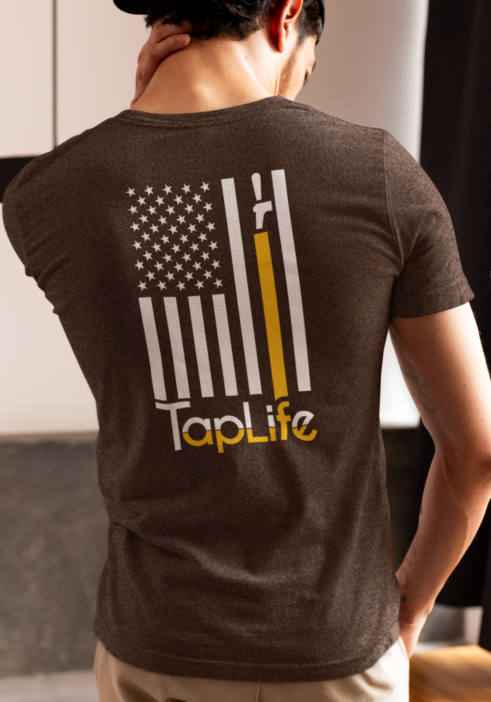 Man wearing heather brown t-shirt with print of American flag, with one stripe yellow pouring from a beer tap, Tap Life logo below