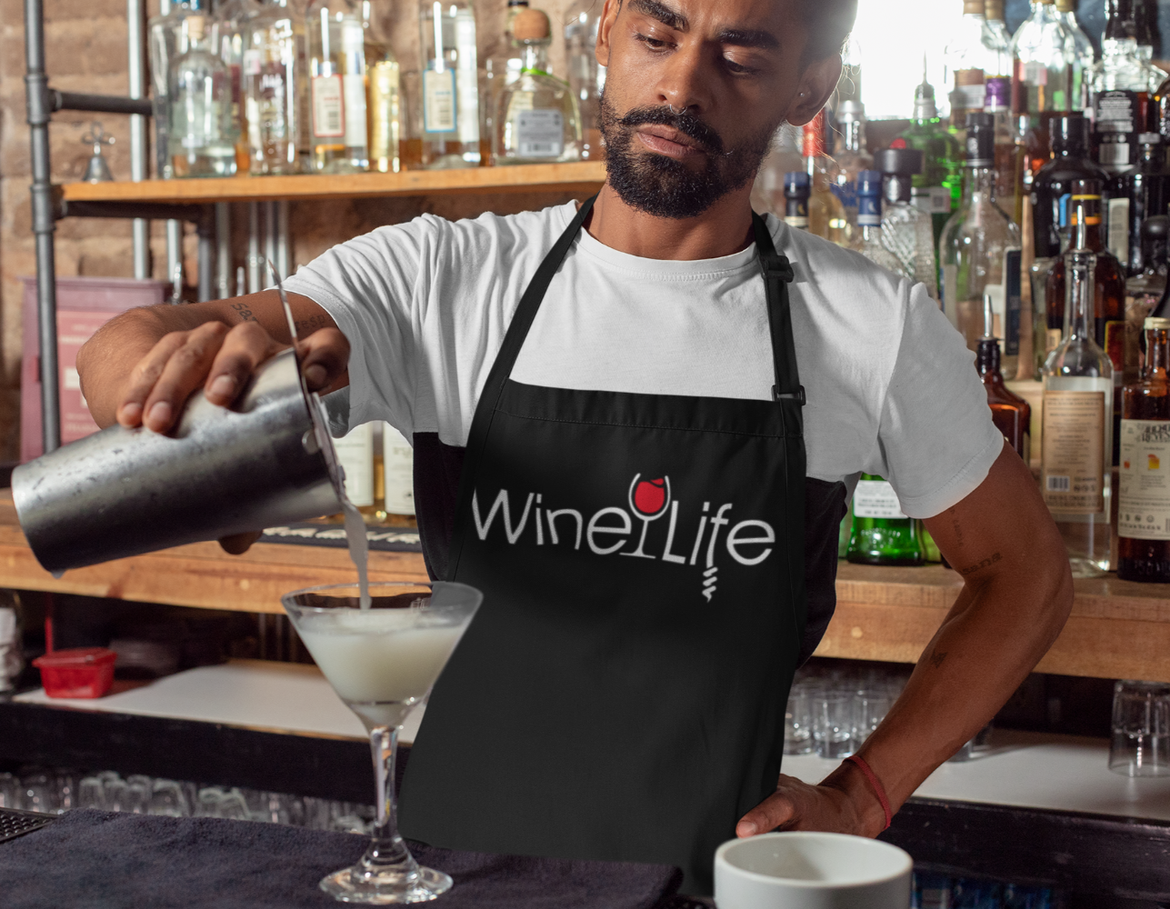 Man mixing a cocktail while wearing a black apron, with a graphic design of the red Wine Life logo across the front.