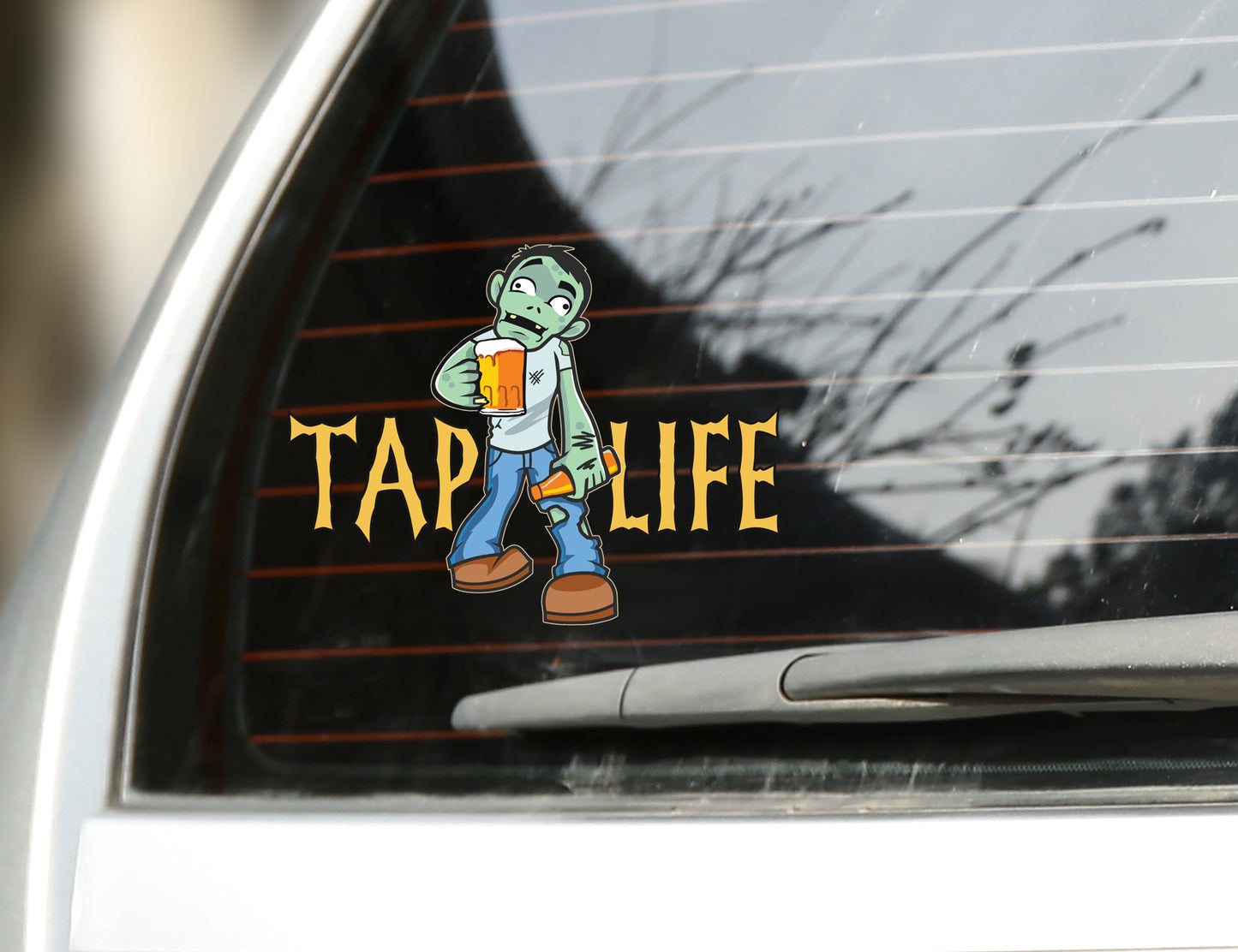 Rear car window with sticker decal of cartoon zombie holding beer mug and bottle of beer, with tap life logo in spooky font.