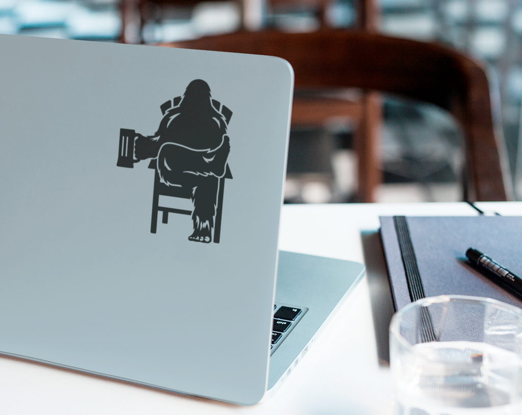 Laptop computer with black decal of Bigfoot relaxing in a chair, holding a beer mug.