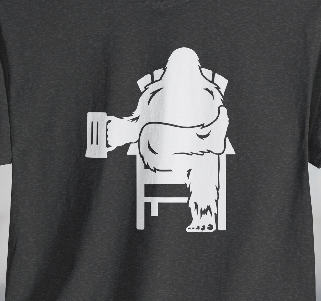 Gray t-shirt with white graphic of Bigfoot holding a beer mug, sitting in a lawn chair with leg crossed in relaxed position.