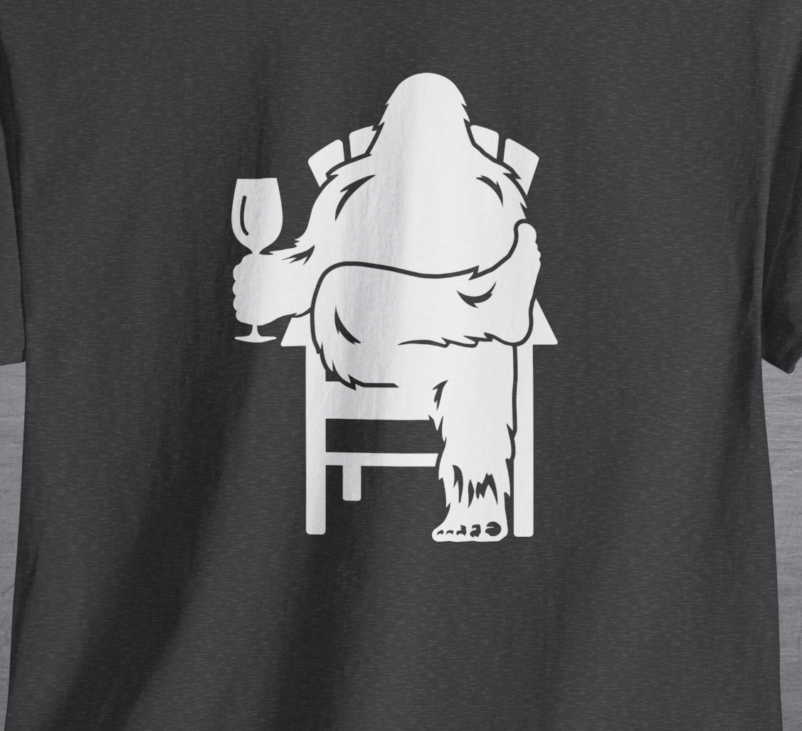 Charcoal gray shirt with graphic design of Bigfoot holding a wine glass, while sitting in a lawn chair relaxing