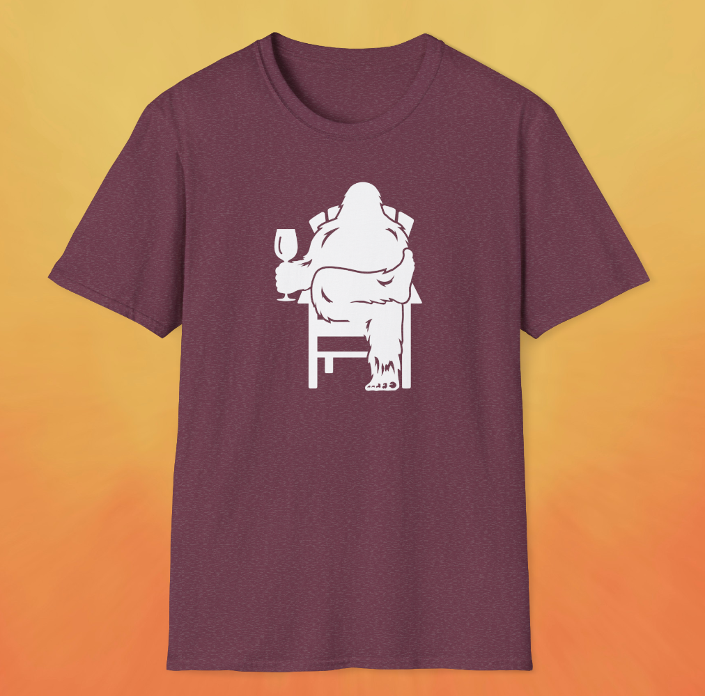 Heather red maroon t-shirt with white print of Bigfoot relaxing in a chair and enjoying a glass of wine.