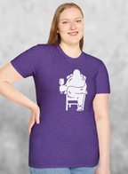 Woman wearing Heather purple t-shirt with white print of Bigfoot relaxing in a chair and enjoying a glass of wine.