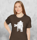 Woman wearing heather brown t-shirt with white graphic of Bigfoot relaxing in a chair and enjoying a mug of beer.