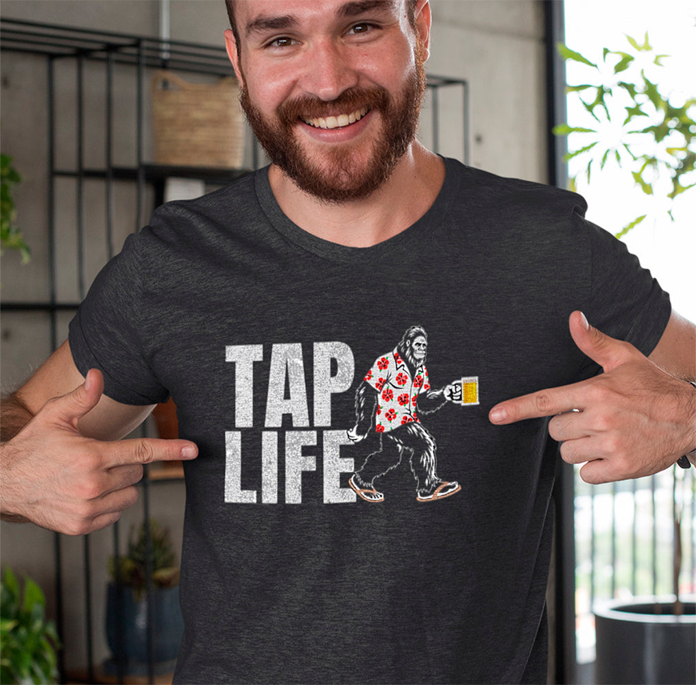 Man wearing a charcoal gray t-shirt with 'Tap Life' text and Bigfoot wearing a Hawaiian shirt and holding a beer