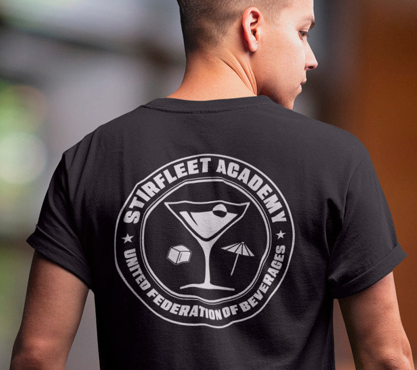 Woman wearing black t-shirt, with white United Federation of Beverages Stirfleet Academy logo, martini glass ice cube umbrella graphic on back of shirt.