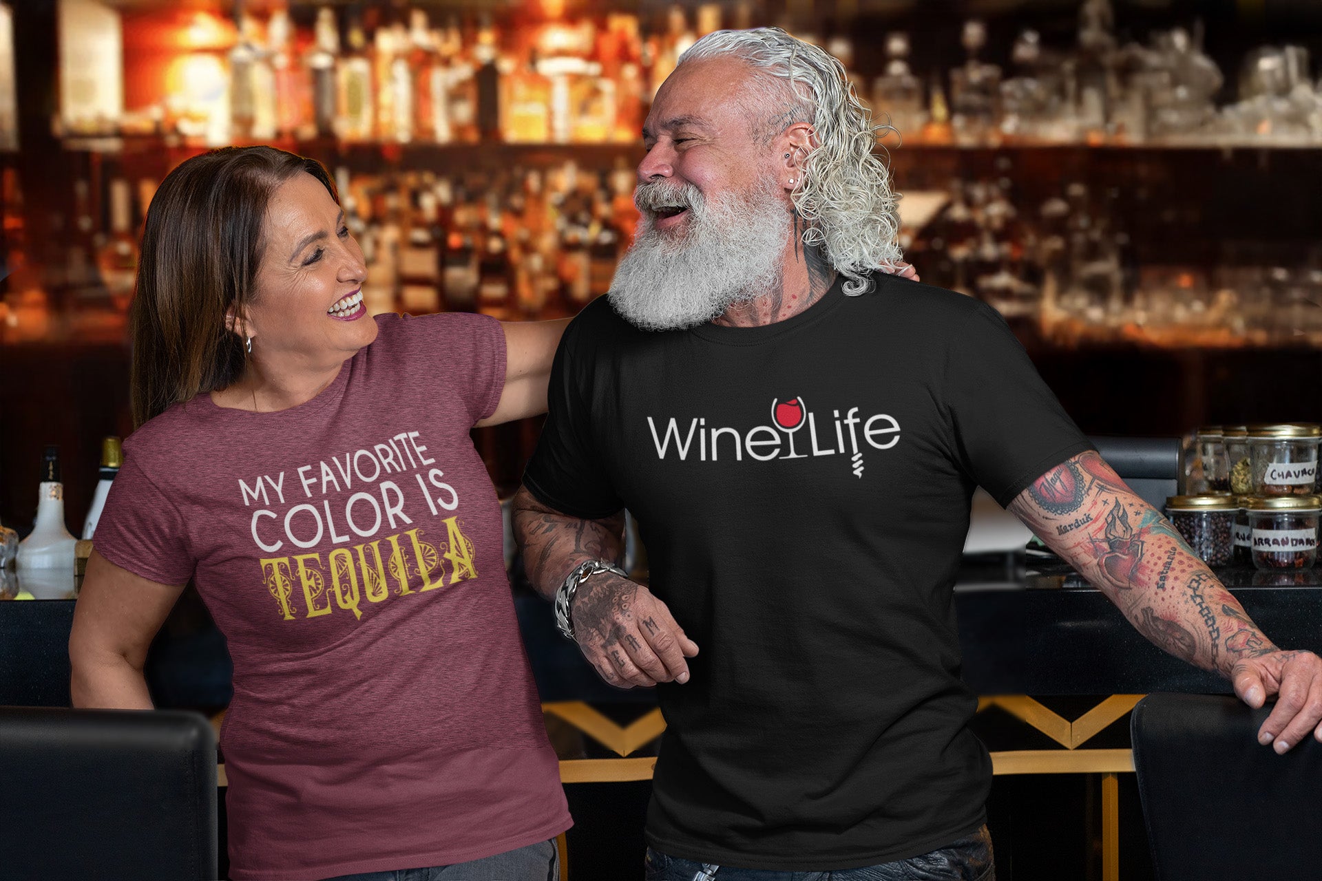 Two people at a bar, man wearing Wine Life t-shirt and woman wearing t-shirt that says "My Favorite Color is Tequila"