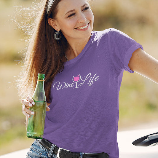 Woman wearing a heather purple t-shirt with wine life written in swirly script letters, and a glass of pink rose' wine
